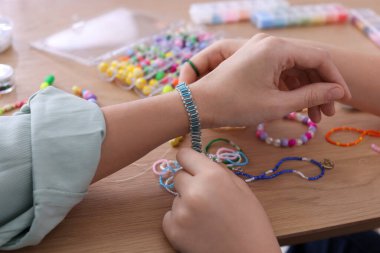 Anne ve kızı masada boncuklu mücevher yapıyorlar, yakın plan.