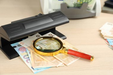 Euro banknotları ve ahşap masanın üzerinde büyüteçle modern para birimi detektörü. Para inceleme aygıtı