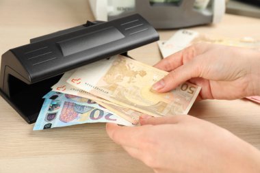 Bir kadın, ahşap masada Euro banknotlarını detektörle kontrol ediyor. Yakın plan. Para inceleme aygıtı