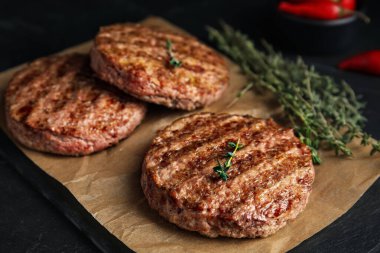 Lezzetli ızgara hamburger köfteleri, siyah masada kekik, yakın plan.