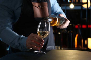 Barmen beyaz şarabı şişeden bardağa dolduruyor.