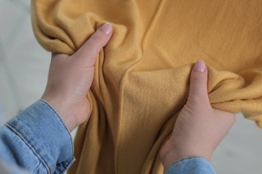 İçerideki yumuşak sarı kumaştan yapılmış elbiselere dokunan kadın, yakın plan.