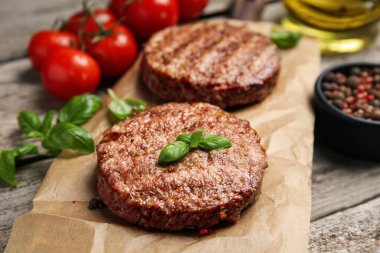 Lezzetli ızgara hamburger köfteleri, kiraz domatesleri ve ahşap masada baharatlar, yakın plan.