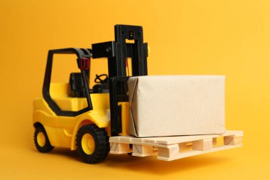 Ahşap paletli oyuncak forklift ve turuncu arka planda kutu.