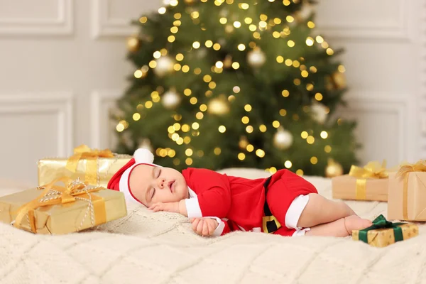 クリスマスの衣装でかわいい赤ちゃんは ぼやけたお祝いのライトに対してニットブランケットで寝ています 冬休み — ストック写真