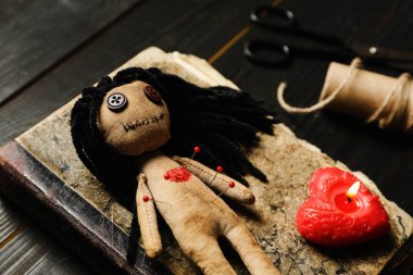 Voodoo bebeği. İğneler, kitap ve kalp şeklinde mumlar, ahşap masa, yakın plan.