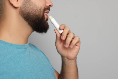Gri arka plana dudak kremi süren genç adam, yakın plan.