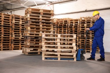 Depoda manuel forkliftle ahşap paletler taşıyan bir işçi.