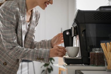 Genç bayan ofiste modern makineyle taze aromatik kahve hazırlıyor.