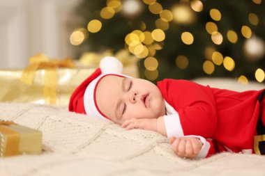 Noel kostümlü şirin bir bebek, bulanık ışık altında örülmüş battaniyede uyuyor. Kış tatili