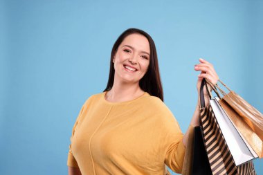 Turkuaz arka planda alışveriş torbaları olan şişman, güzel bir kadın.