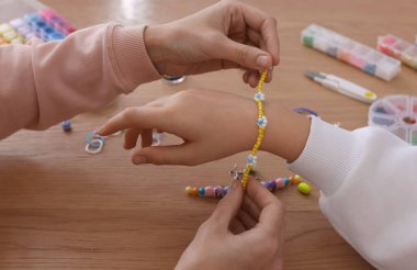 Anne ve kızı masada boncuklu mücevher yapıyorlar, yakın plan.