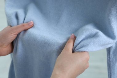 Yumuşak, açık mavi kumaştan yapılmış elbiselere dokunan kadın iç mekanda, yakın plan.