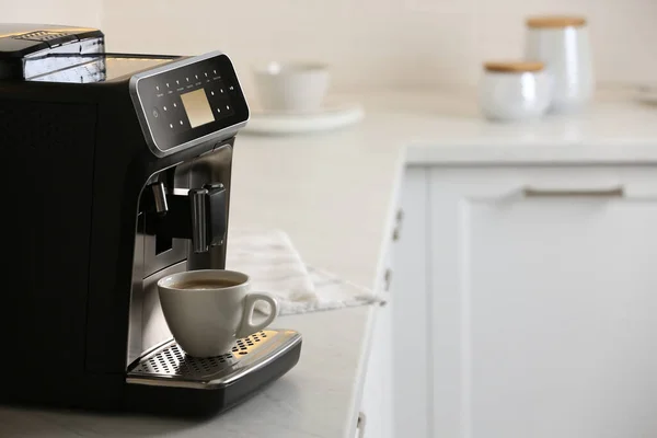 Modern electric espresso machine with cup of coffee on white marble countertop in kitchen
