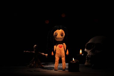 Kalpli bir kadın voodoo bebeği ve karanlıkta masada tören malzemeleri.