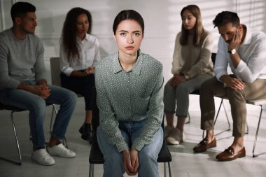 Mutsuz genç bir kadın ve arkasından iş çeviren bir grup insan. Terapi seansı