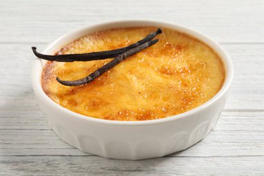 Lezzetli creme brulee ve vanilya çubukları beyaz ahşap masada, yakın çekim görüntüsü