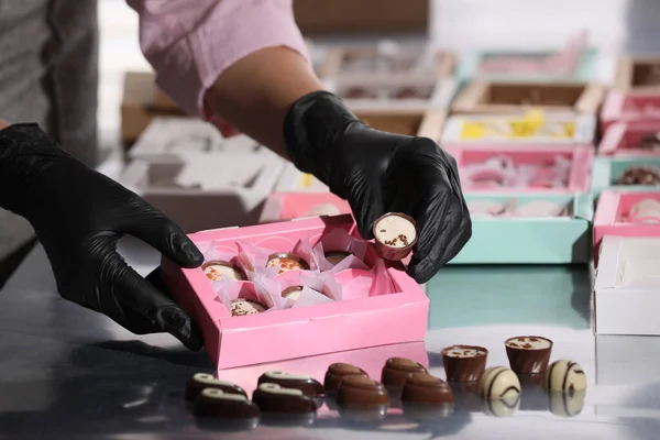Woman packing delicious candies into pink box at production line, closeup
