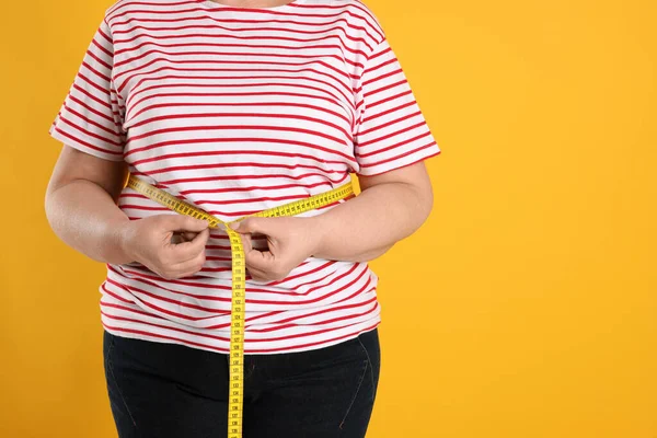 肥胖妇女用橙色背景的带子测量腰围 — 图库照片
