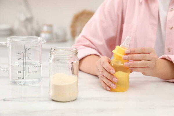 Woman preparing infant formula at table indoors, closeup. Baby milk