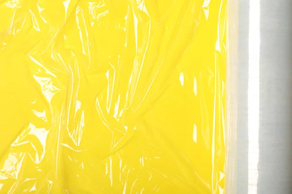 Roll of plastic stretch wrap film on yellow background, top view