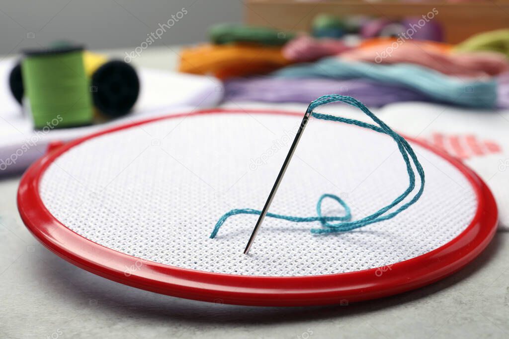 Embroidery hoop with fabric and needle on light grey
