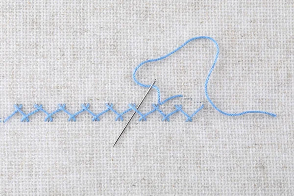 キャンバス上のライトブルーの糸と針で作られた刺繍ステッチ トップビュー — ストック写真