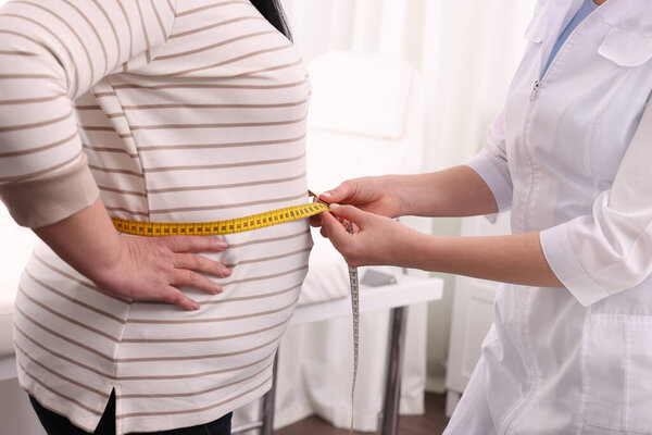 Питатель измеряет избыточный вес женской талии лентой в клинике, крупным планом