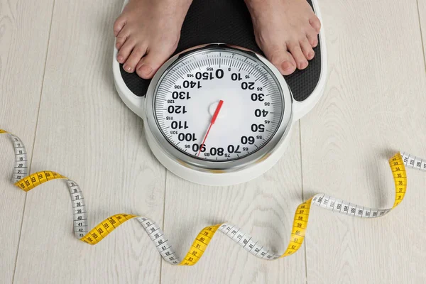 Closeup of woman using scales on floor near measuring tape, above view. Overweight problem
