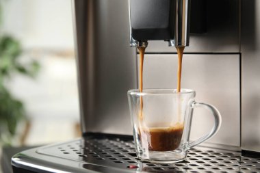Espresso makinesi cam bardağa kahve dolduruyor. Arka plan bulanık, yakın plan. Metin için boşluk