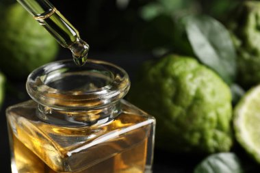 Siyah masanın üzerindeki cam şişeye bergamot yağı damlatıyor.