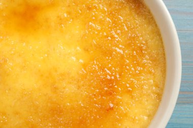 Açık mavi ahşap masada seramik ramekin içinde leziz krema brulee, yakın plan.