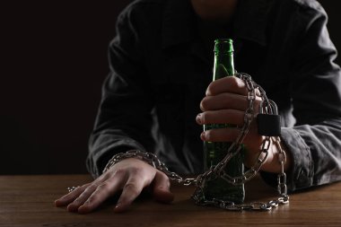 Alkol bağımlılığı. Ahşap masaya bira şişesiyle zincirlenmiş bir adam, yakın plan.