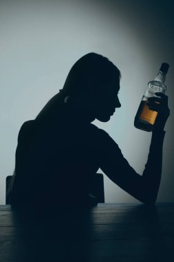 Alkol bağımlılığı. Ahşap masada elinde viski şişesi olan bir kadın silueti.