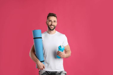 Yoga minderi ve pembe arka planda titreyen yakışıklı bir adam.