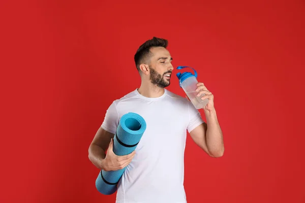 Stilig Man Med Yogamatta Dricksvatten Röd Bakgrund — Stockfoto