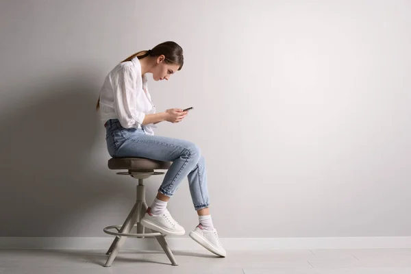 Mulher Com Postura Usando Smartphone Enquanto Sentado Banquinho Perto Parede — Fotografia de Stock