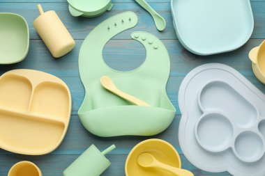 Açık mavi ahşap arka planda silikon bebek önlüğü ve plastik bulaşık takımı ile düz kompozisyon