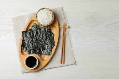 Kuru nori çarşafları, pilavı, soya sosu ve çubukları beyaz ahşap masa üzerinde, üst manzara. Metin için boşluk