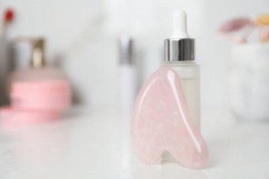 Rose Quartz gua sha aracı ve kozmetik ürünü beyaz masada, yakın plan. Metin için boşluk