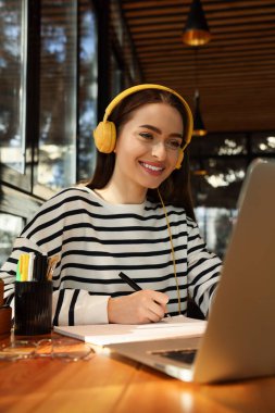 Laptop ve kulaklıklı genç kız öğrenci kafede ders çalışıyor.