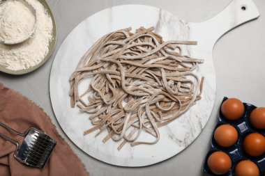 Pişmemiş ev yapımı soba (karabuğday eriştesi) ve gri masadaki malzemeler, düz konum
