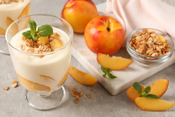 Şeftalili yoğurt, granola, nane ve açık gri masada meyveler.