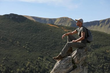 Sırt çantalı turist kayalık zirvede dağ manzarasının tadını çıkarıyor