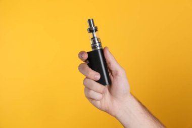 Sarı arka planda elektronik sigara tutan adam, yakın plan.