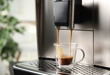 Espresso makinesi cam bardağa kahve dolduruyor. Arka plan bulanık, yakın plan. Metin için boşluk