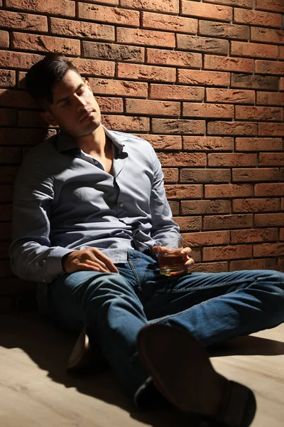 赤レンガの壁の近くの床に座っているアルコール飲料のガラスと中毒の男 — ストック写真
