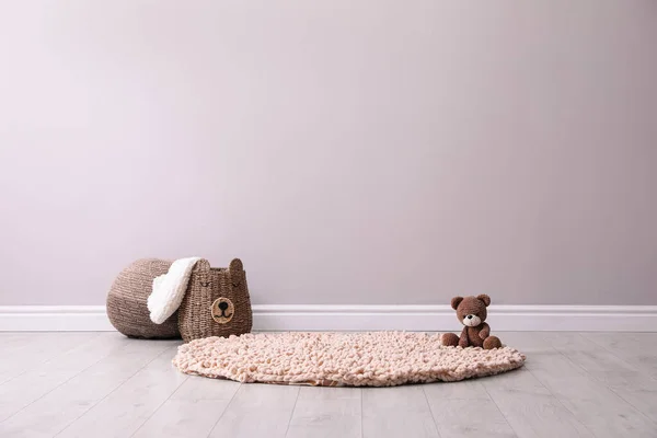 Toy bear and wicker basket near light grey wall in child room. Interior design