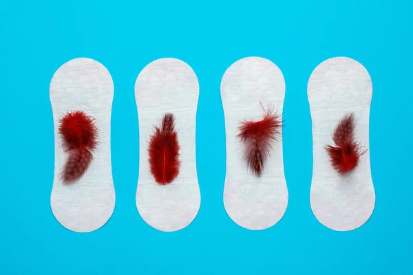 Menstrual pads with red feathers on light blue background, flat lay