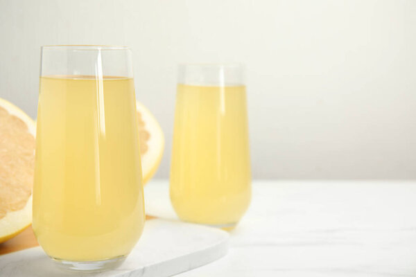 Glasses of fresh pomelo juice on white table. Space for text